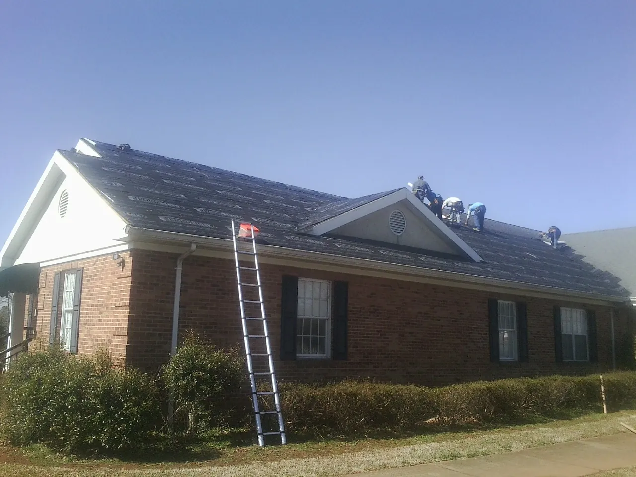 Crew tearing shingles off a brick ranch roof with a ladder set — Metal Roof Repair work by our crew in Perryman