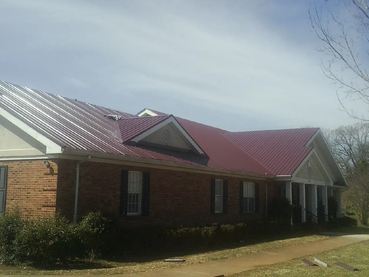 Red metal roof with gabled entries on a long brick building, from a Hail Damage Roof Repair job in Perryman