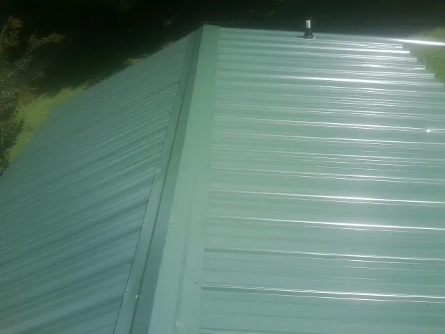 New green metal panels meeting at the ridge of a roof — Flat Roof Repair work by our crew in Perryman