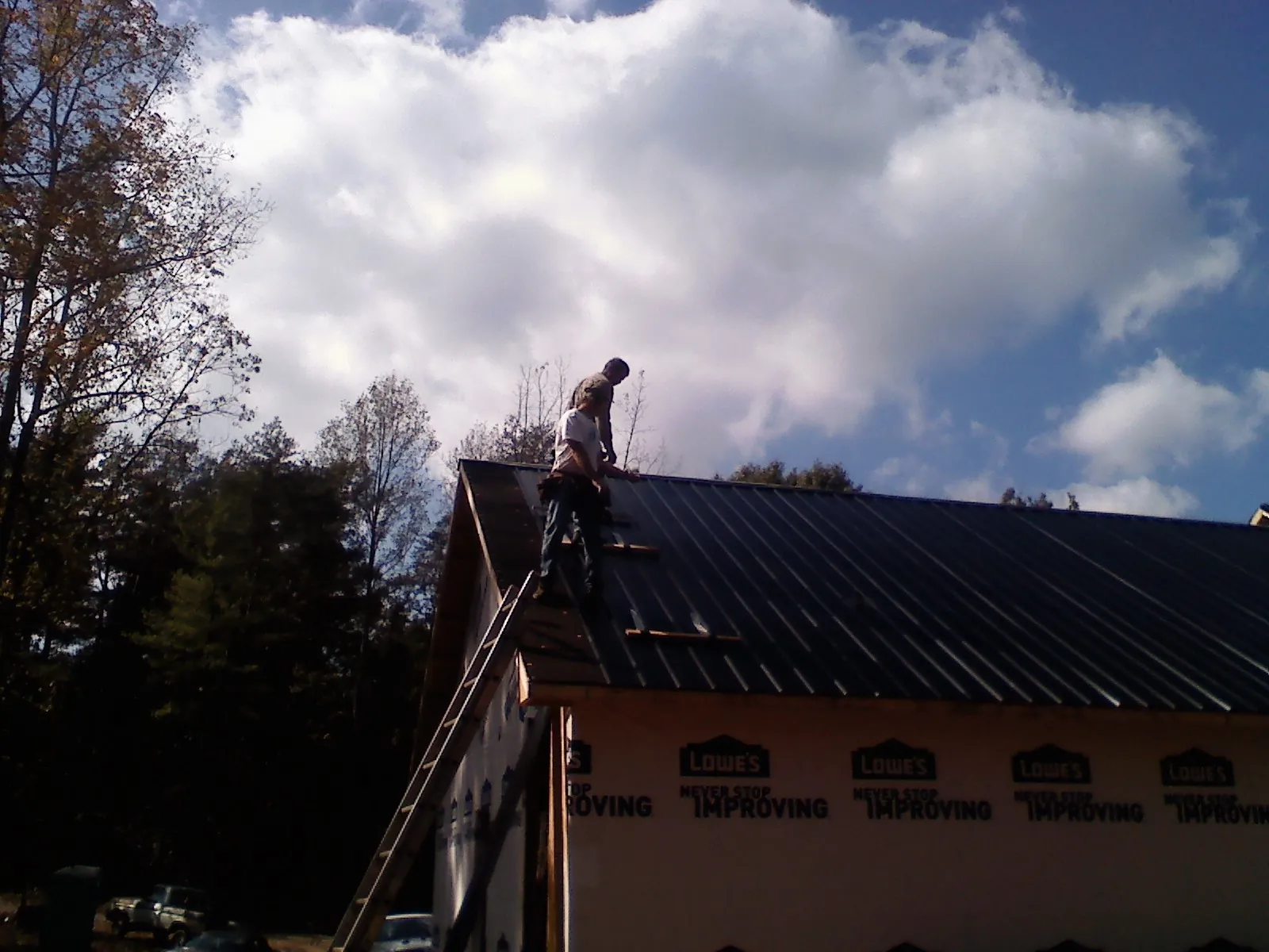 Roofer fastening dark metal panels high against a cloudy sky, from a Roof Inspection job in Perryman
